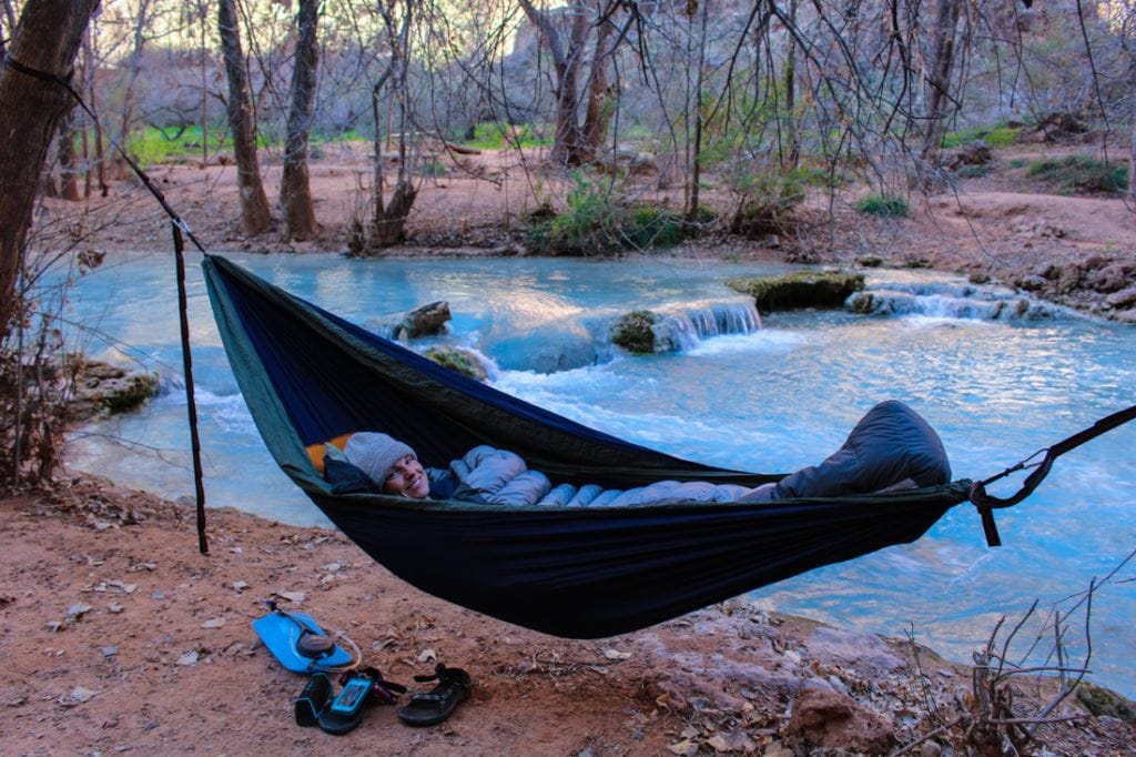 A woman sleeping in a hammock next to a turquoise river