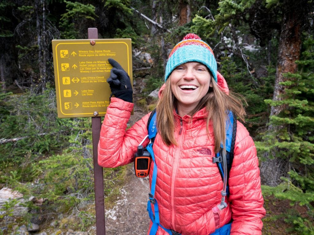 Kristen pointing to a trail sign with Garmin inReach attached to backpack strap