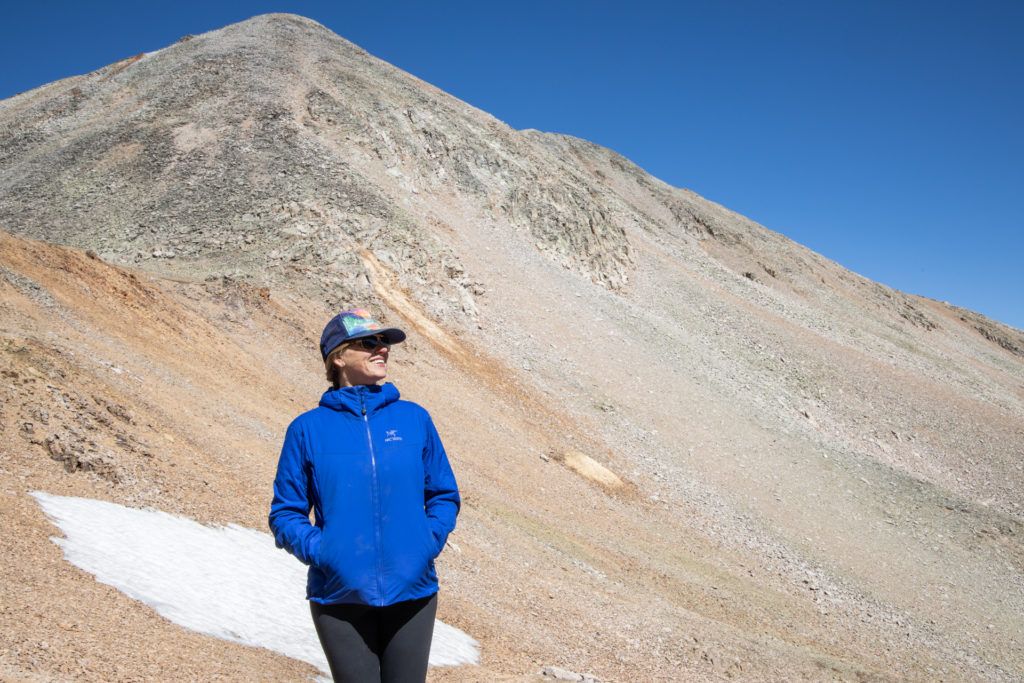 Kristen wearing Arc'teryx Atom hoody with tall, barren Colorado peak behind her