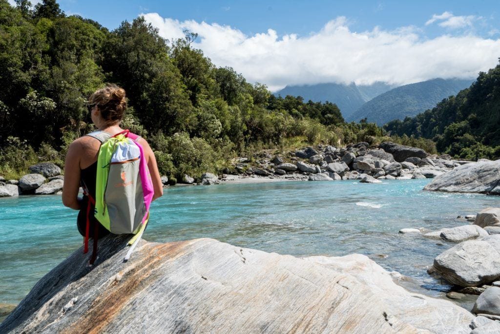 徒步旅行者坐在靠近水的大岩石上，穿着色彩鲜艳的科多帕希吕宋日包