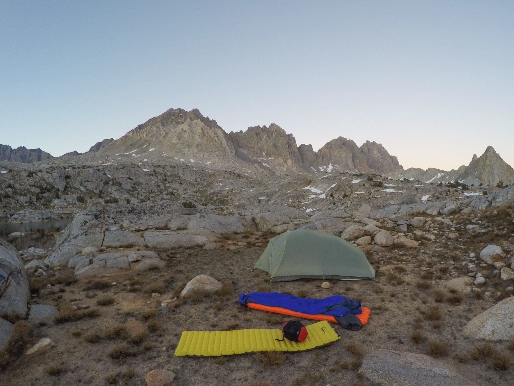 尼莫·张张的睡袋放在外面，旁边是一个背包睡袋和帐篷，远处是崎岖不平的山脉