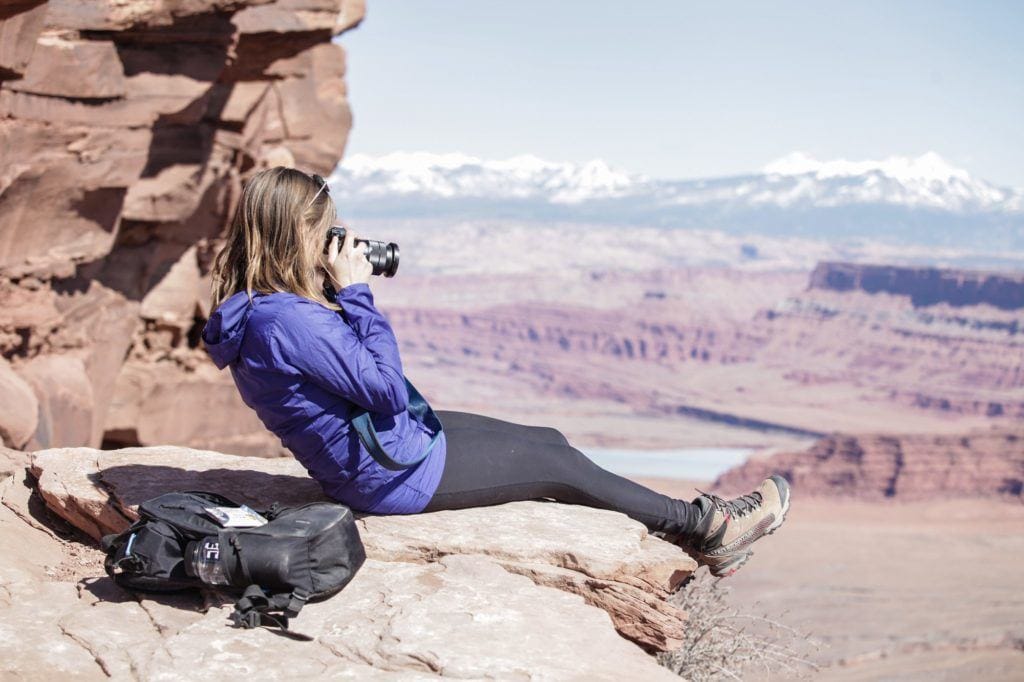 克里斯汀坐在犹他州的岩壁上，在峡谷上拍照