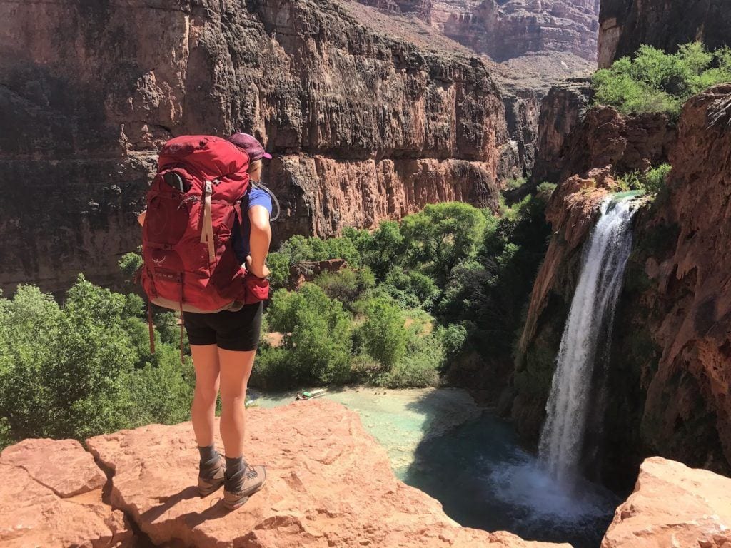 Woman standing on a cliff overlooking Havasu Falls with a red backpacking pack on