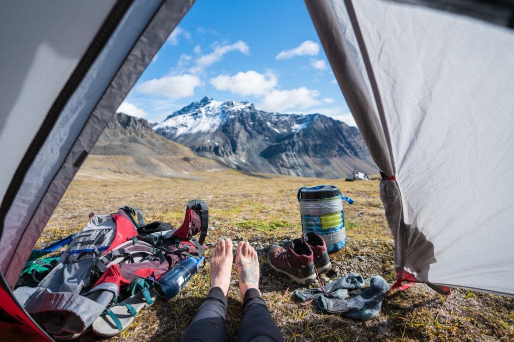 A pair of feet hanging out of a backpacking tent with mountains in the distance,