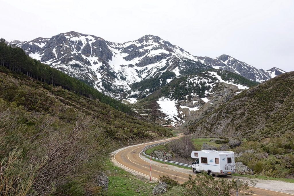 An RV campervan driving a windy road in front of snowy mountains in the distance