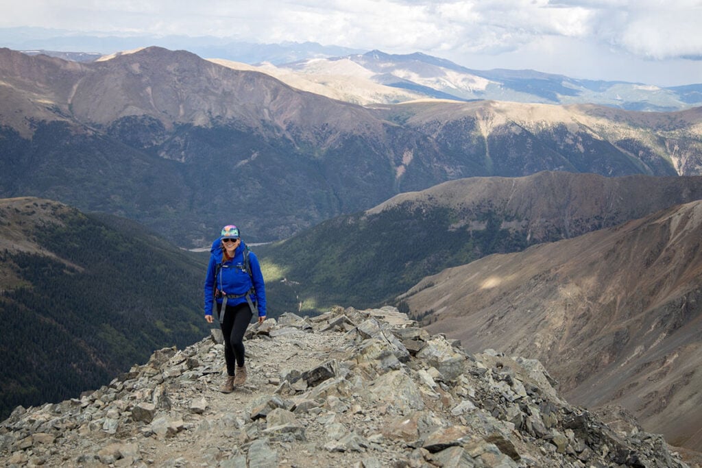 Kristen hiking on rocky trail in Colorado with tall mountain ranges in the background