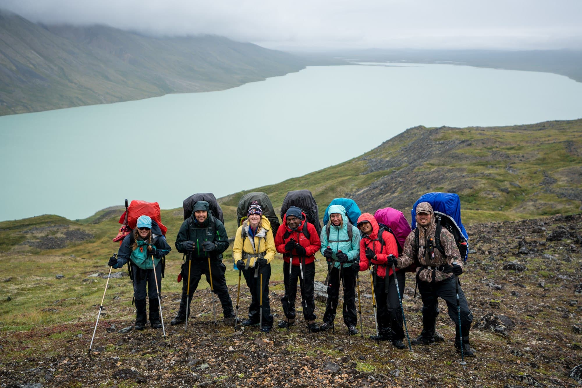 一群微笑的徒步旅行者站在阿拉斯加的一个湖前。下雨了，他们穿着雨衣。