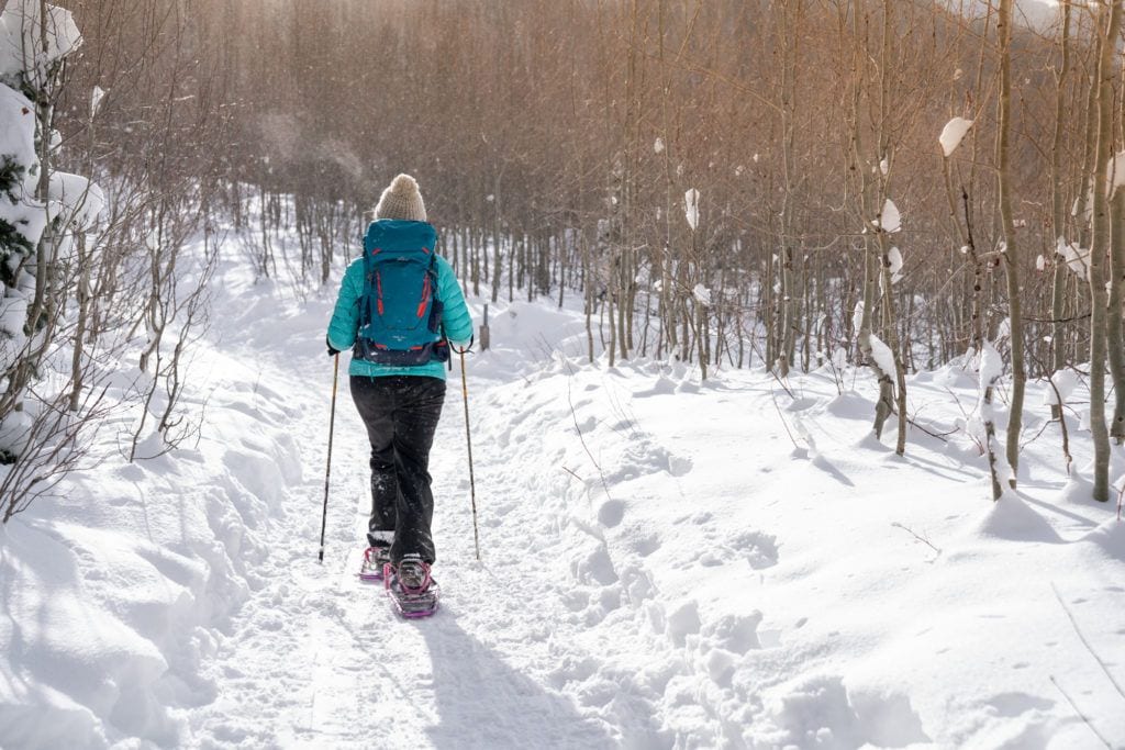女人穿雪鞋在雪道穿过树林