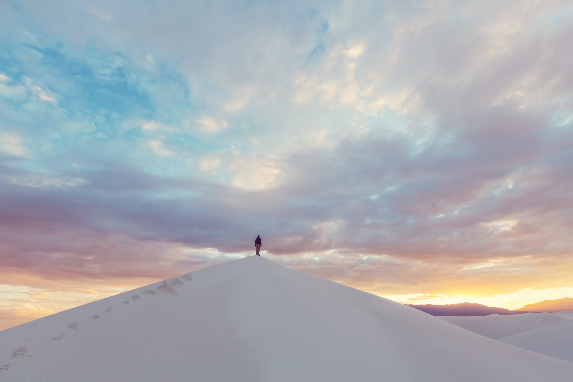 人们站在白沙国家公园的大沙丘上，头顶上是五彩缤纷的日落天空