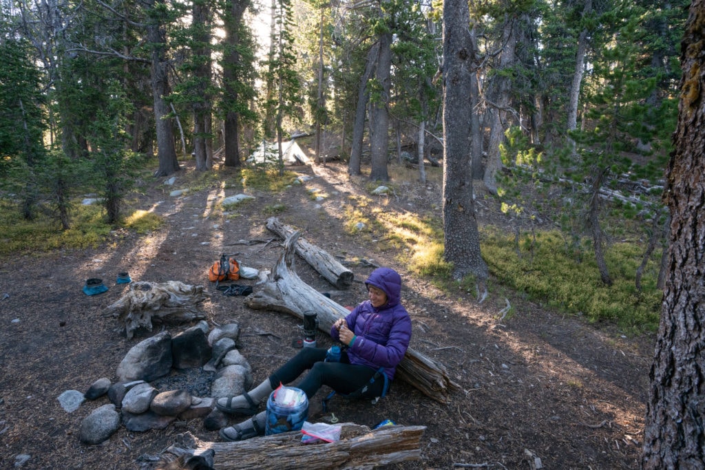 女人坐在地面上的野外露营地与岩石火圈和周围的森林