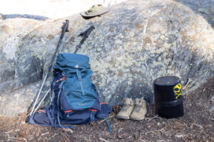 背包装备，包括背包、登山杖、靴子和防熊筒，靠在岩石上