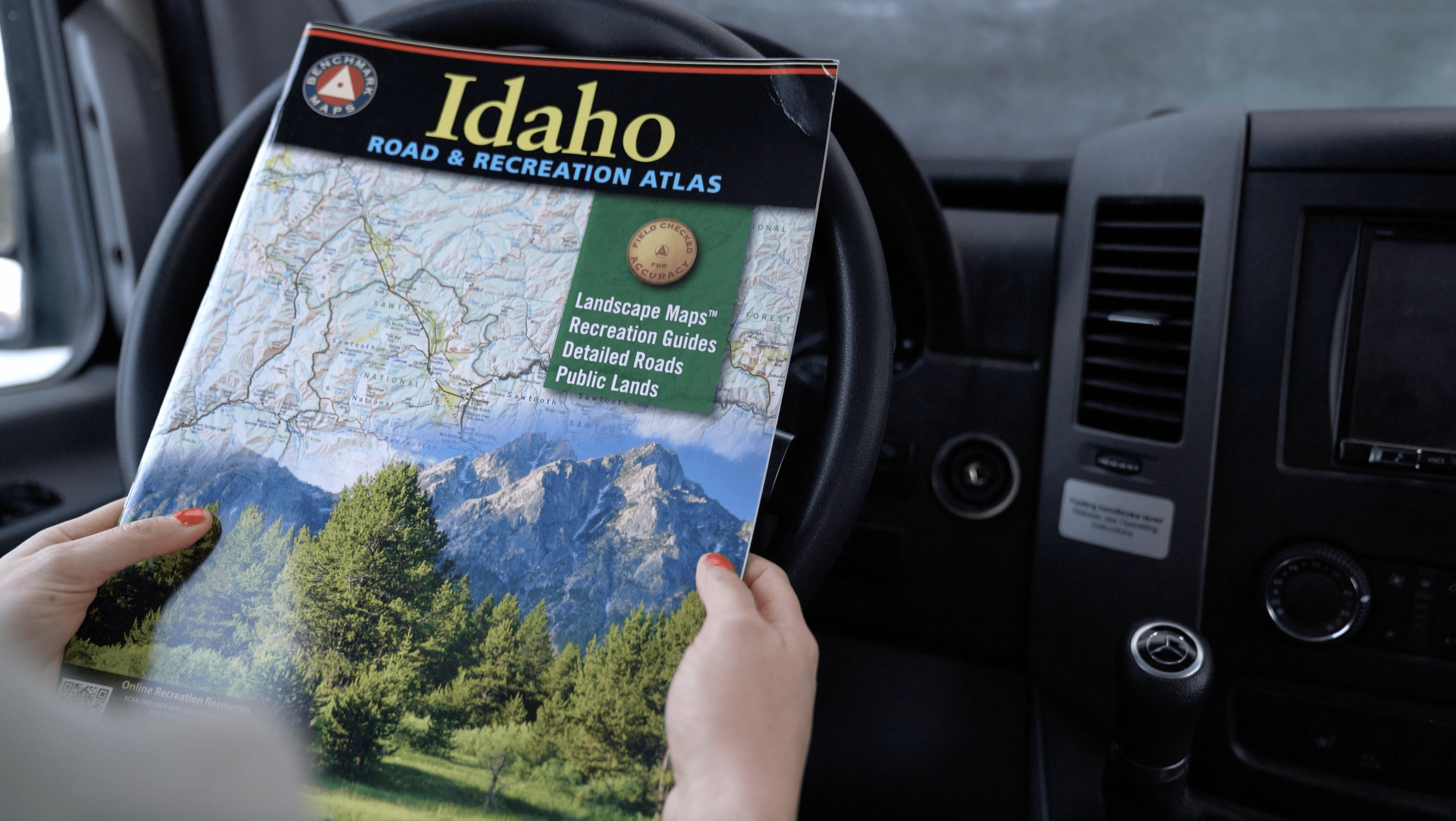 a person holds a Benchmark Road Atlas in the driver's seat