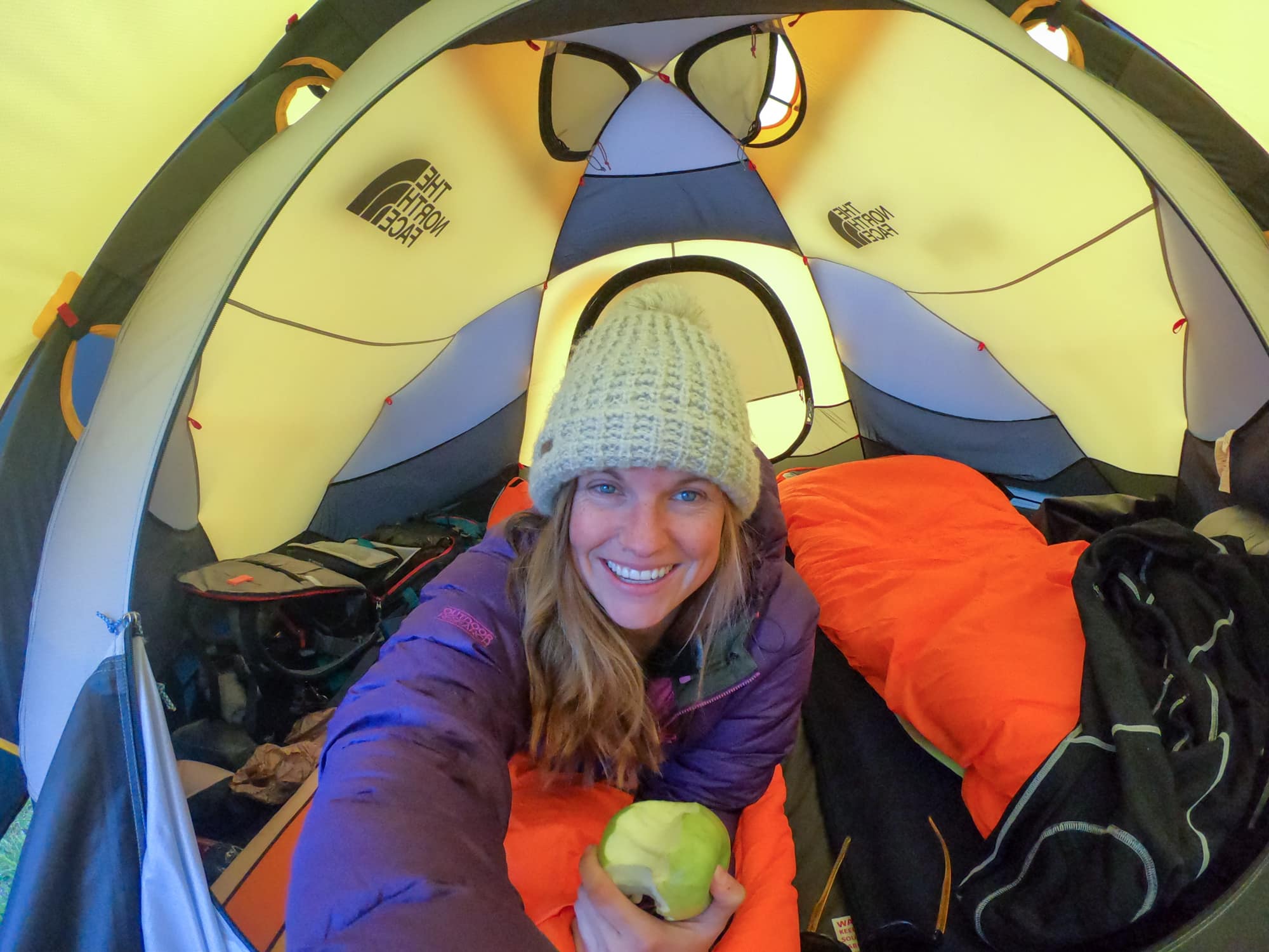 克里斯汀穿着暖和的衣服，在帐篷里一边吃着苹果一边自拍