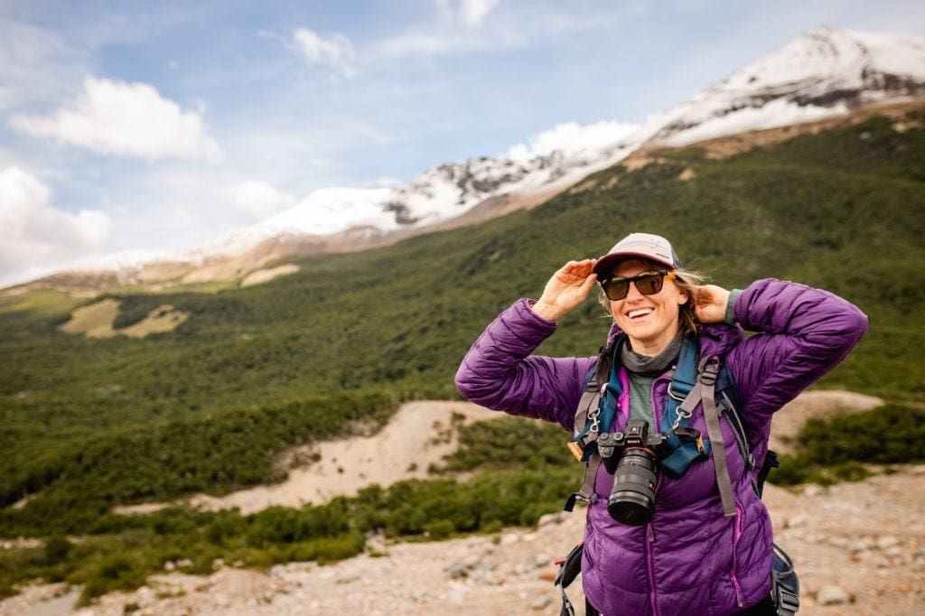 Woman smiling for photo on hiking trail. She's wearing a camera around her neck