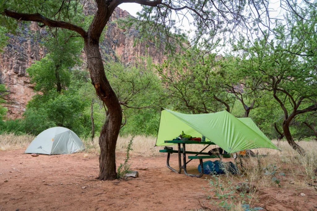 露营地，在树后搭起帐篷，在野餐桌上铺上防水布，在上面放上装备