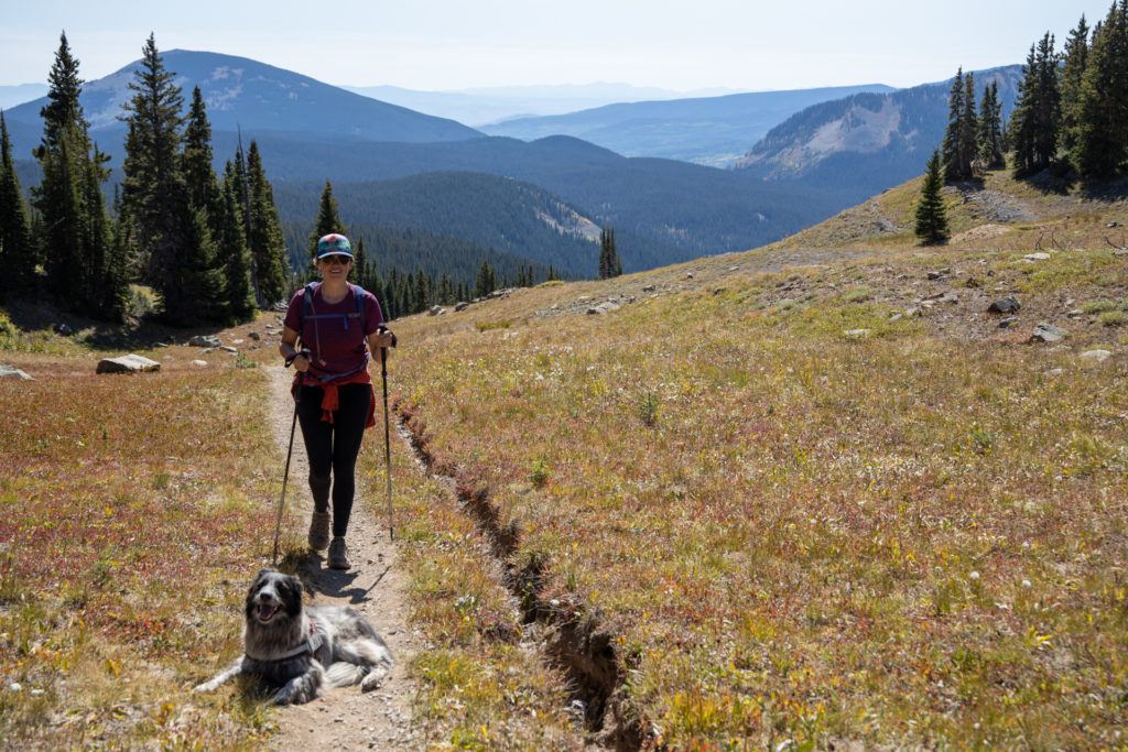 克里斯汀hiking on trail with dog in Colorado with mountains in background