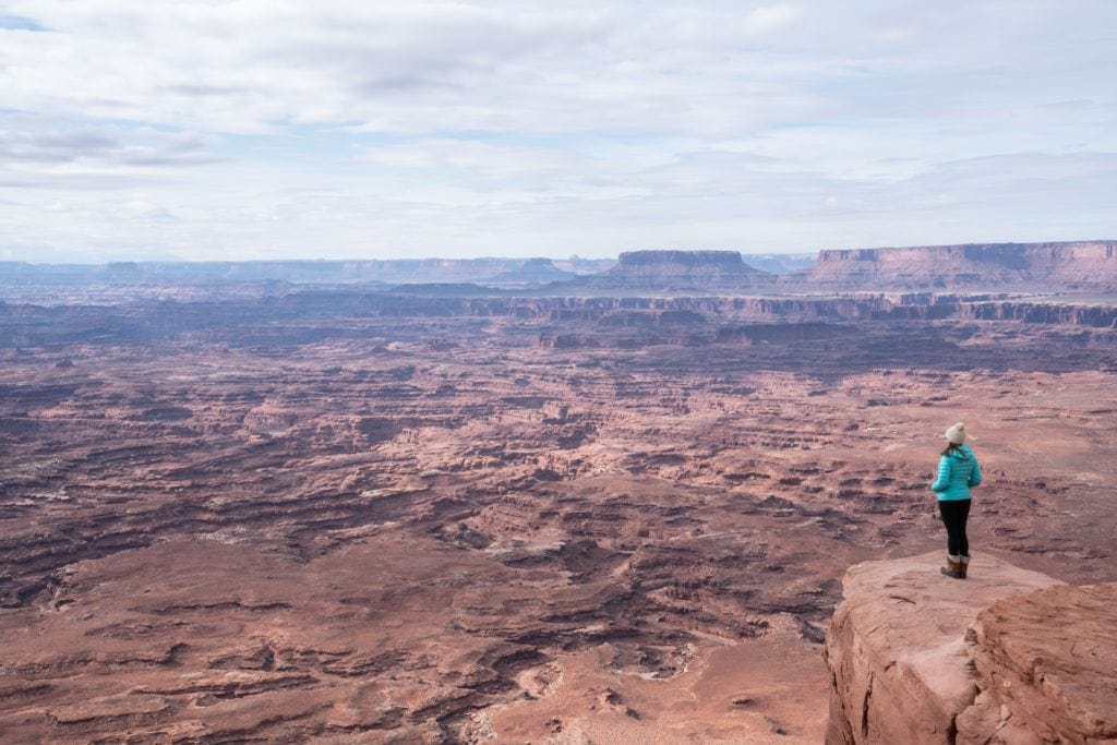 一位女士站在岩石边缘俯瞰峡谷地国家公园