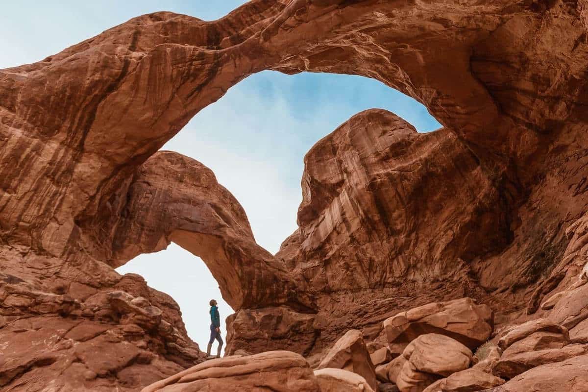 Woman standing under red rock arch looking up at bridge overhead
