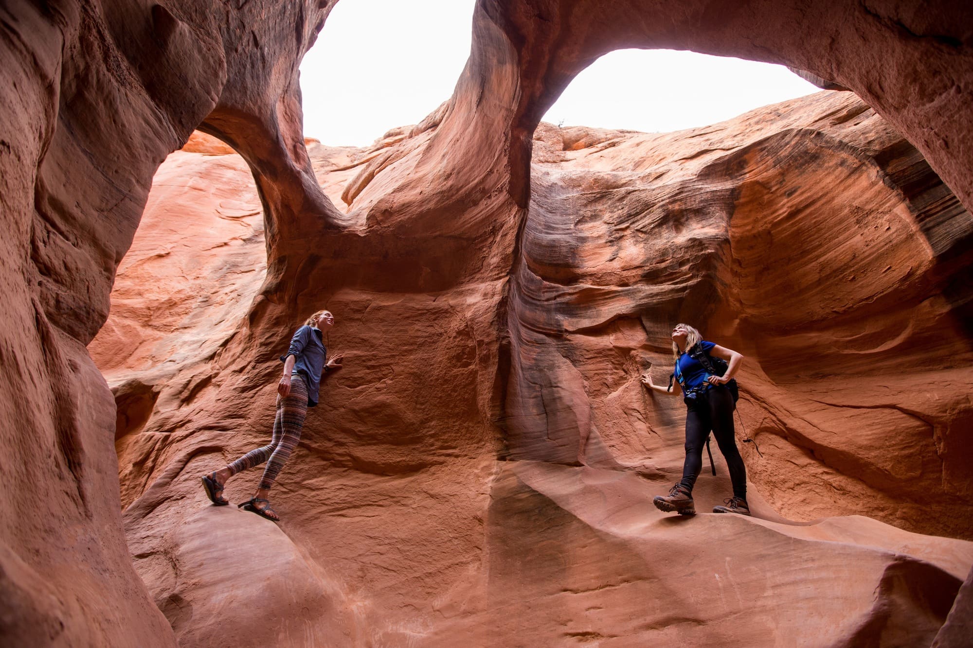 两名女子在犹他州探索有三个天空洞的红色岩石洞穴