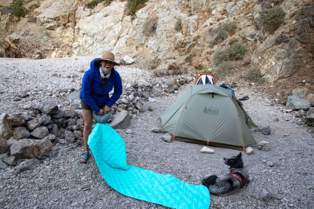 一个女人膨胀leeping pad next to her tent on a backpacking trip