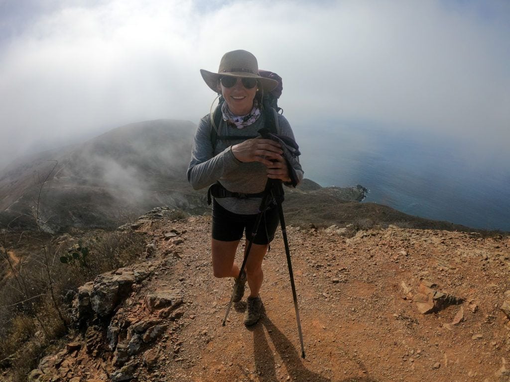 A woman backpacking high in the clouds clutching trekking poles