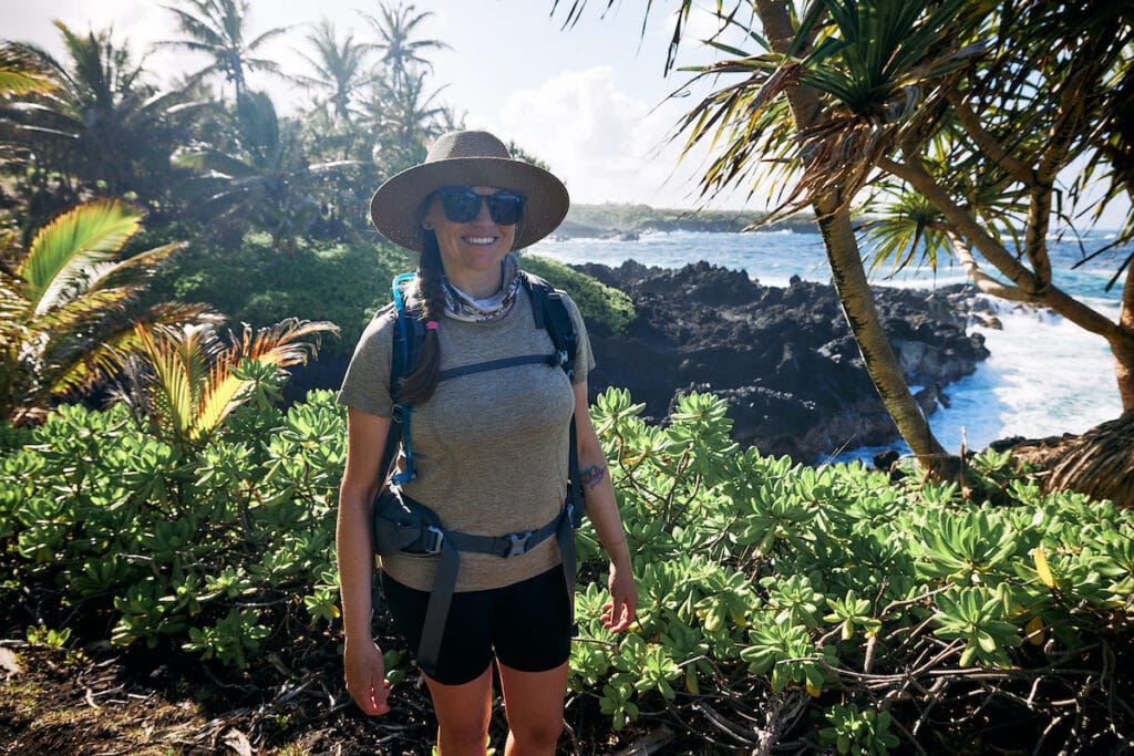 Kristen smiling for photo on hike in Hawaii with ocean and tropical landscape behind her