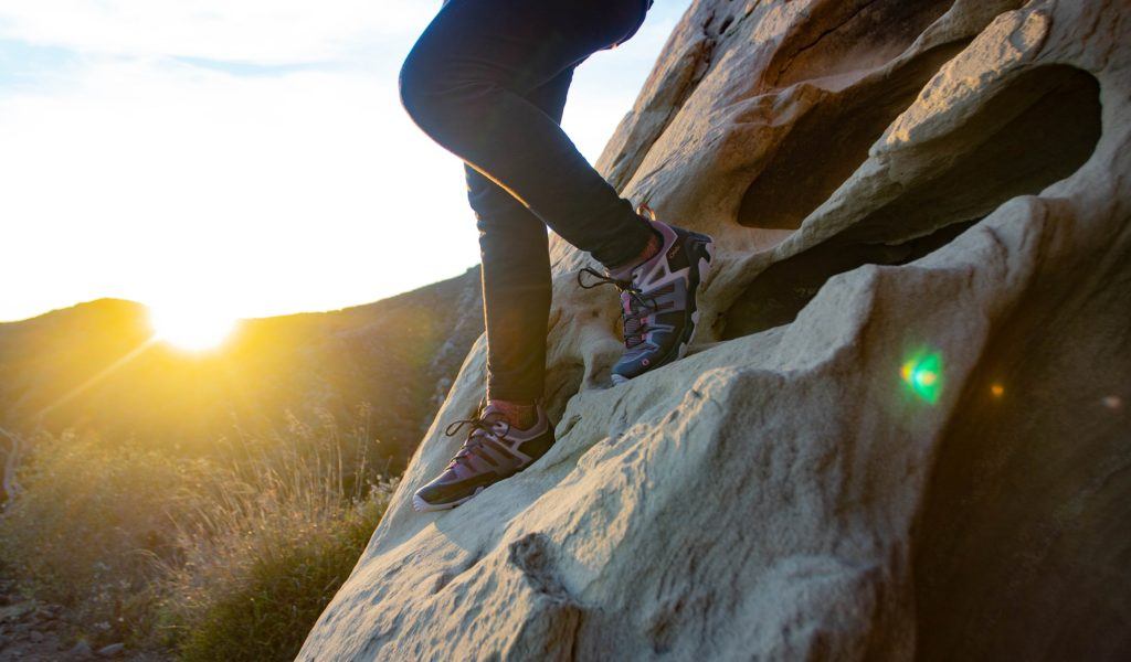 照片显示，一名女子穿着轻便的登山鞋沿着陡峭的岩石板徒步旅行，背景是落日