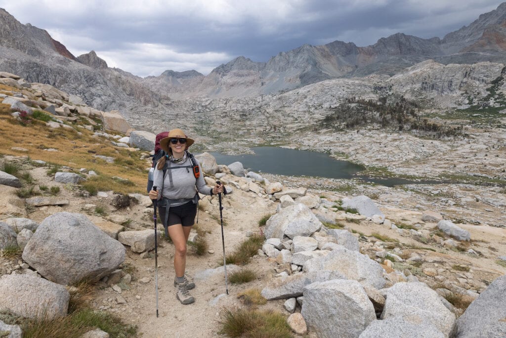 Kristen hiking on trail wearing backpacking pack and holding hiking poles in remote area of California's Sierra Nevada mountains