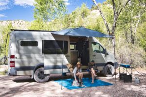 Two people sit outside their Sprinter van using the Moonshade portable awning