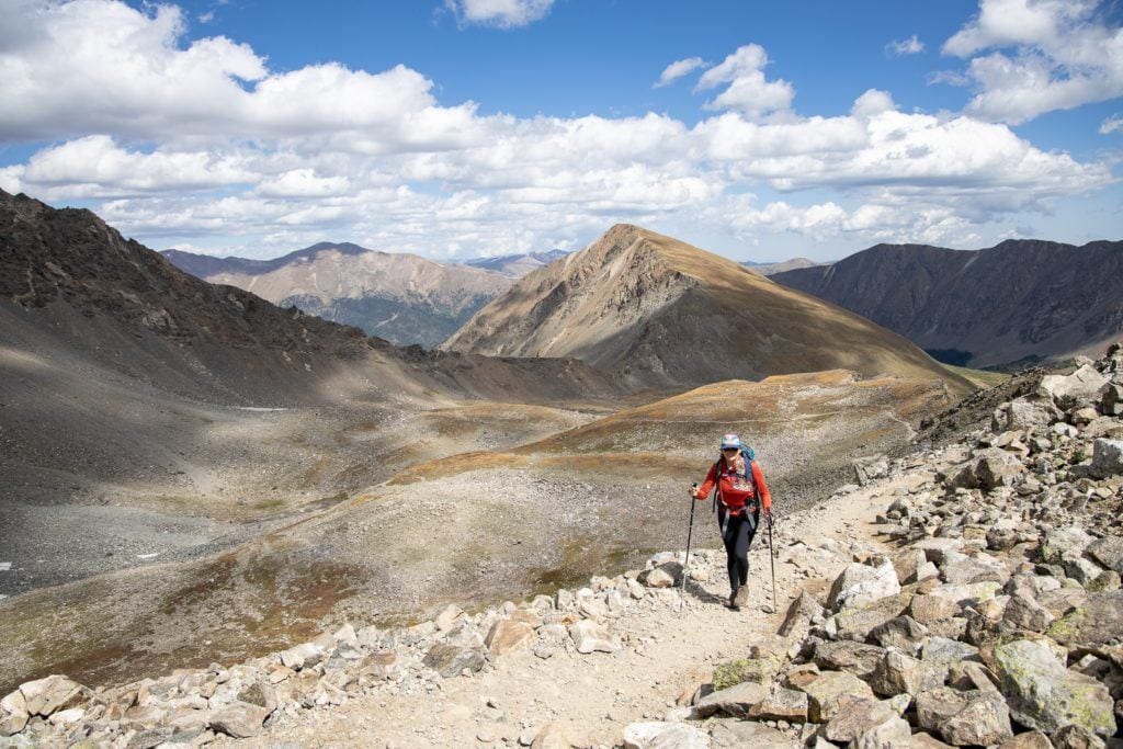Woman hiking on high alpine trail in Colorado using trekking poles and wearing hiking gear