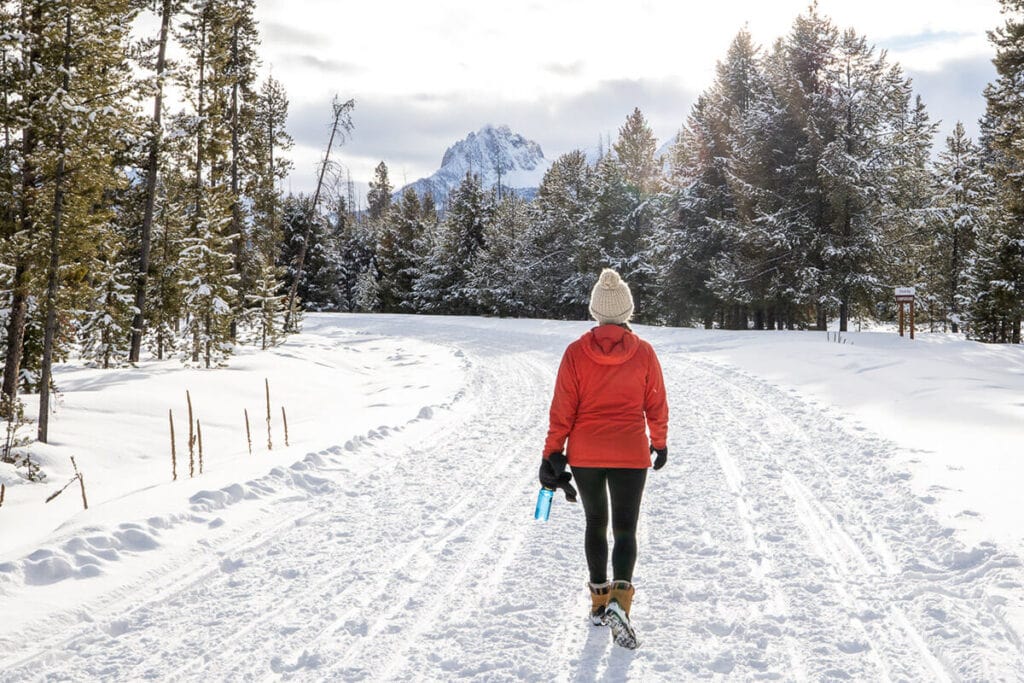 妇女徒步旅行在冬天的雪-探索最好的冬季徒步旅行的衣服，基本装备，并提示在寒冷的天气分层