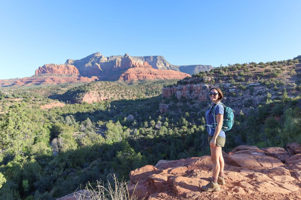 Female hiker wearing day pack posing for photo in Sedona, Arizona with beautiful red rock bluffs in the distance