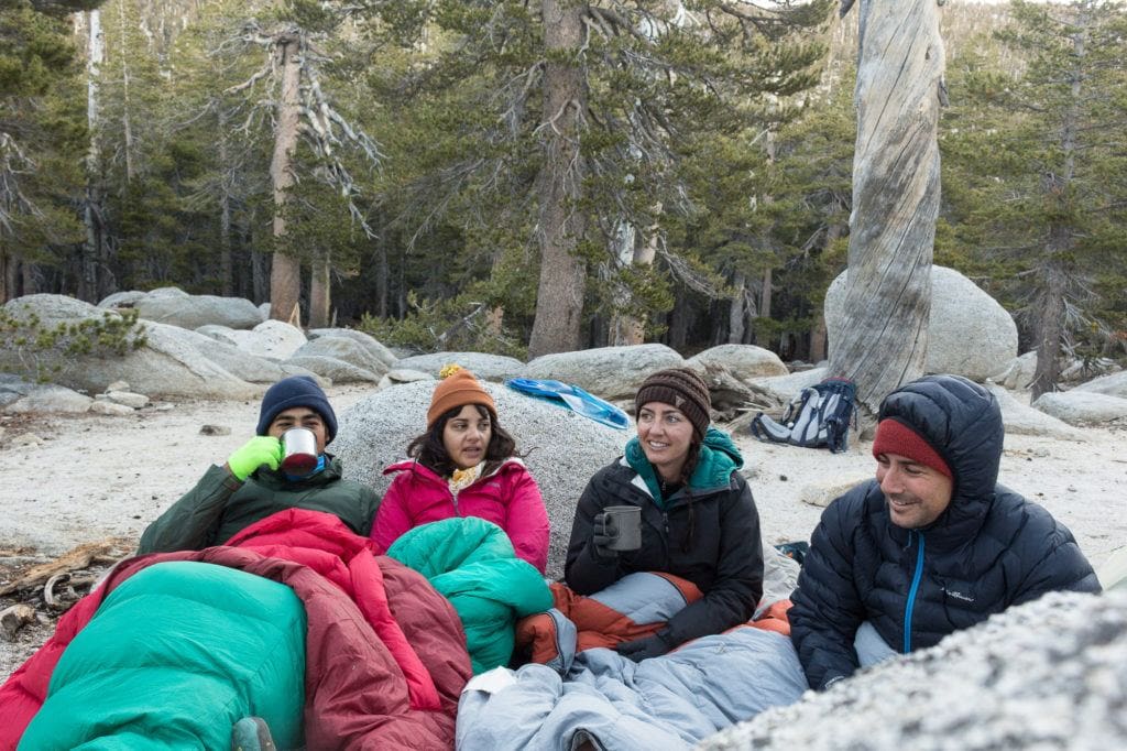 一组四名露营者紧挨着坐在地上，穿着暖和的衣服和睡袋