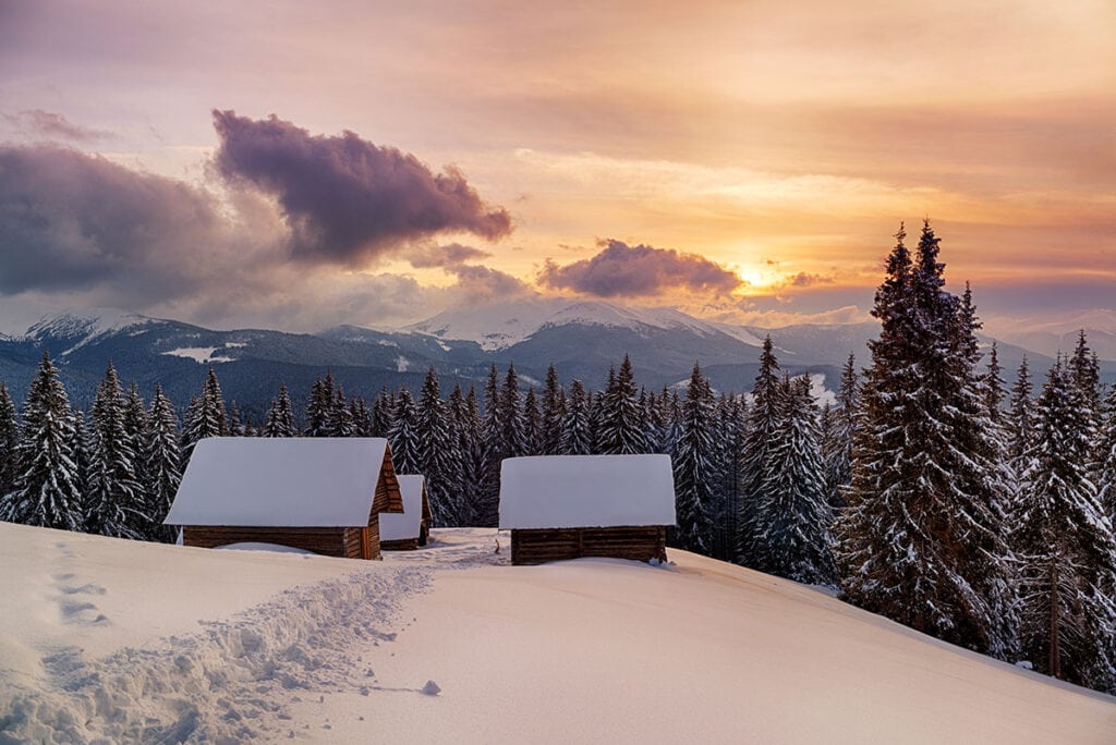冬季偏僻的小屋被雪景包围，太阳在山峰上落山