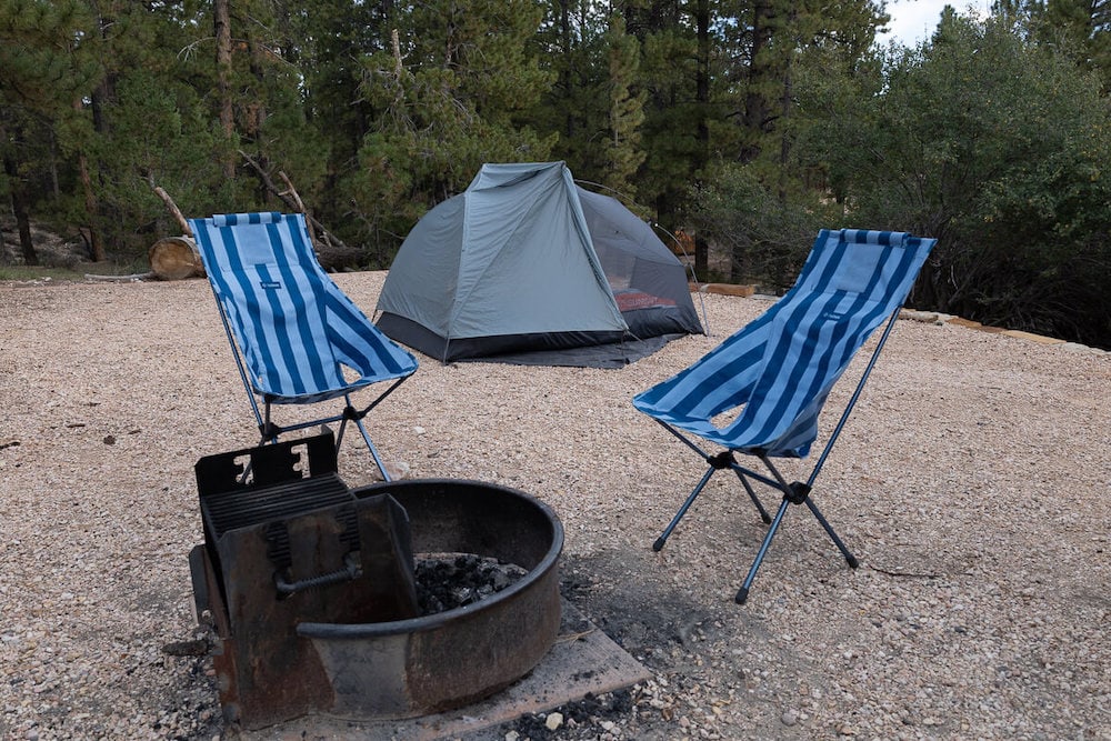 在营地的一个没有点燃的火坑周围有两把露营椅，后面搭着帐篷