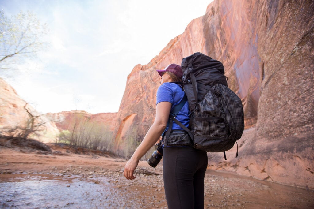一名背包客背着Hyperlite超轻背包前往犹他州的土狼峡谷。女人站在浅水里，两边都是高高的悬崖