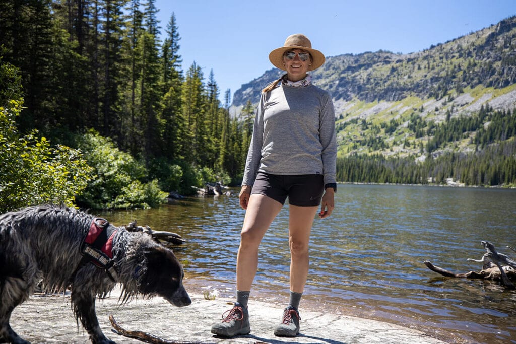 Kristen smiling for photo in front on lake wearing Patagonia Capilene long-sleeve shirt with dog next to her
