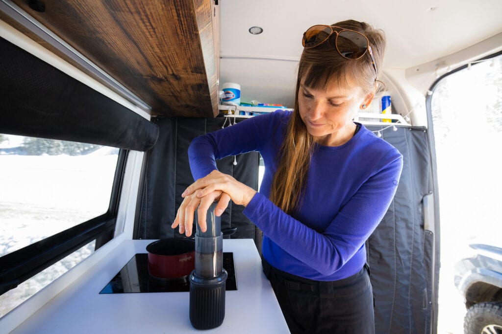 A woman uses the Aeropress Go coffee press in her Sprinter van