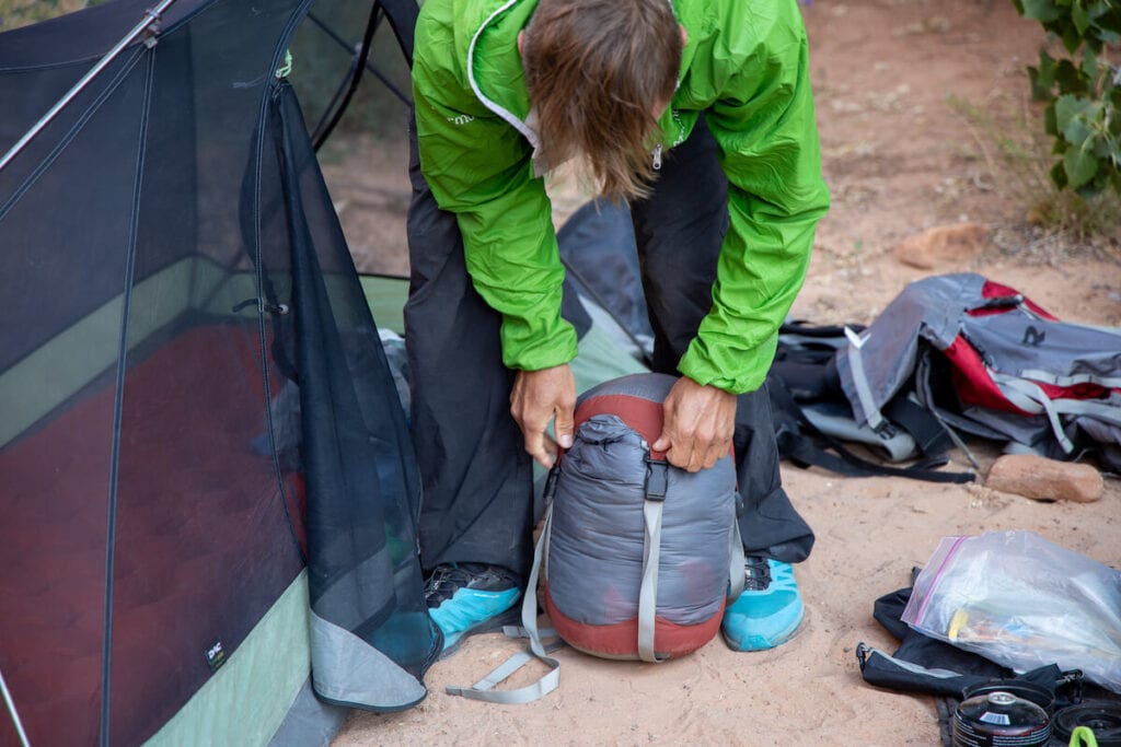 在一次背包旅行中，一名男子将睡袋塞进帐篷旁边的压缩袋中
