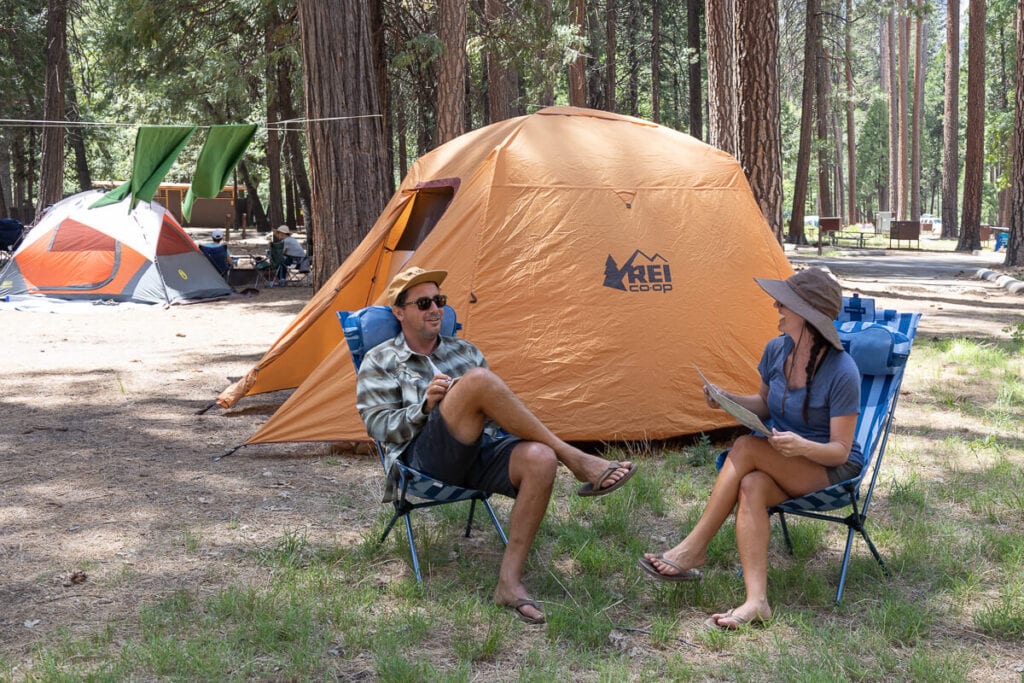 两个人坐在露营地的露营椅上，周围搭着帐篷
