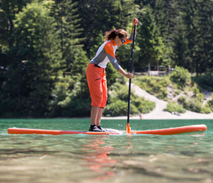 女子站在桨板上，在平静的水面上划桨