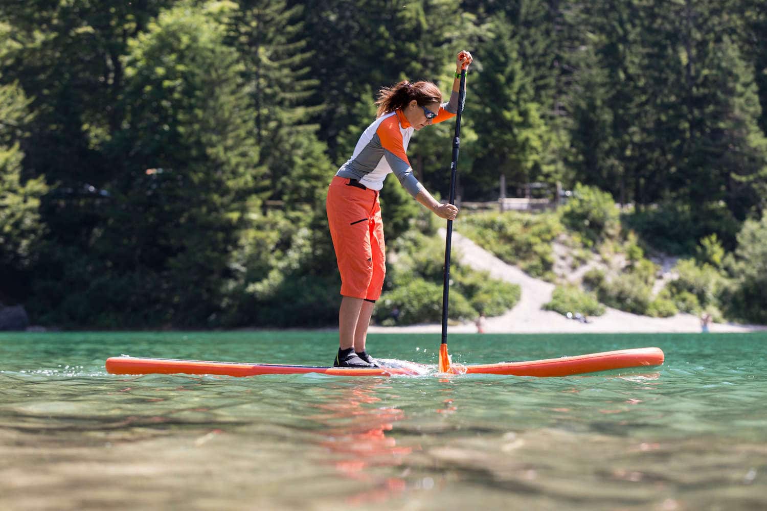 女人站在桨板划桨在平静的水