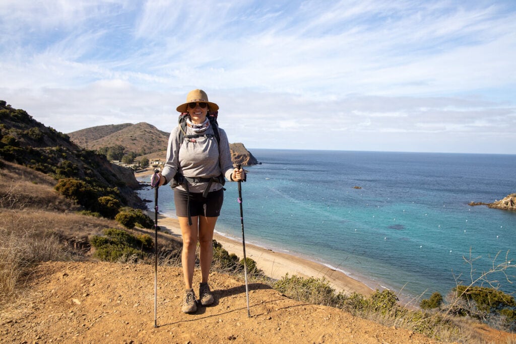 A woman smiles on the Trans Catalina Trail in California. She's wearing the REI Sahara Shade Hoodie and Oboz hiking boots