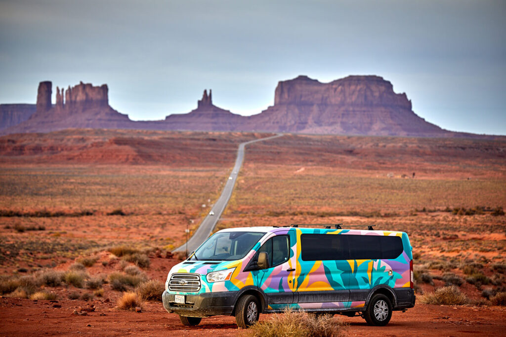 A brightly painted Escape Campervan rental in front of a desert background