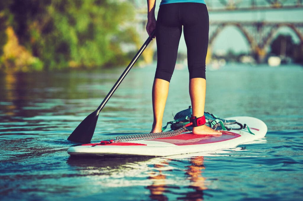 一个女人站在平坦水面上的桨板上