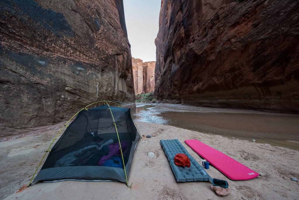 一个在峡谷里搭起的背包帐篷，旁边放着两个背包睡袋