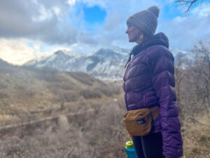 一个女人背着lululmeon腰包，穿着暖和的蓬松夹克，徒步旅行，背景是雪山