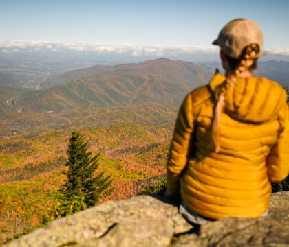 秋天，一位女性徒步旅行者背对着镜头坐在俯瞰斯莫基山国家公园的岩石观景台上