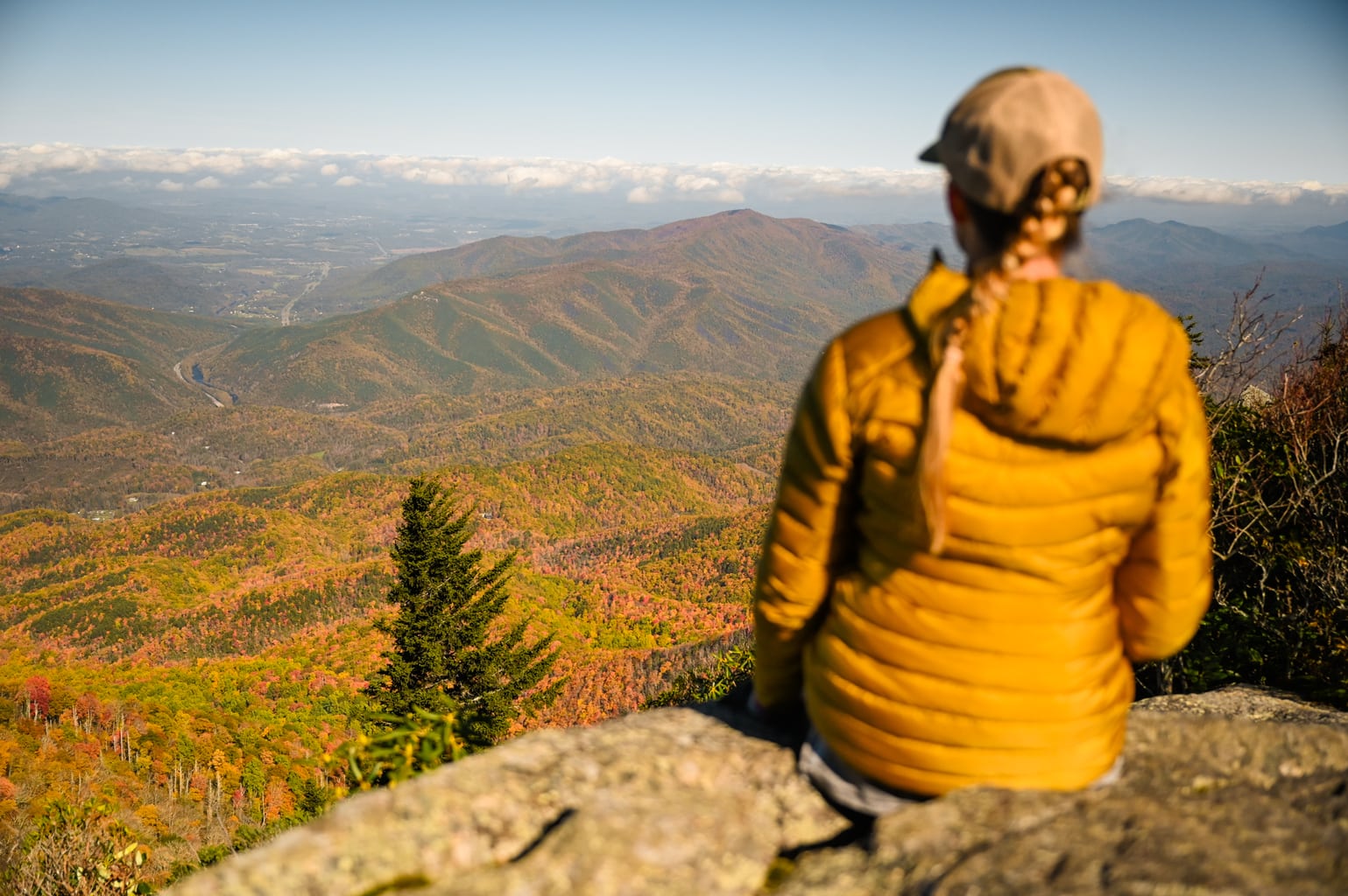 秋天，一位女性徒步旅行者背对着镜头坐在俯瞰斯莫基山国家公园的岩石观景台上