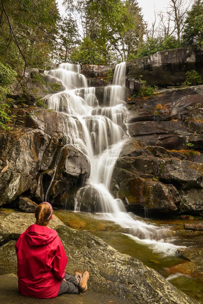女徒步旅行者坐在瀑布底部的岩石上，背对着相机